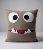Brown plush monster pillow with big white eyes and a pocket mouth for kids room decor.
