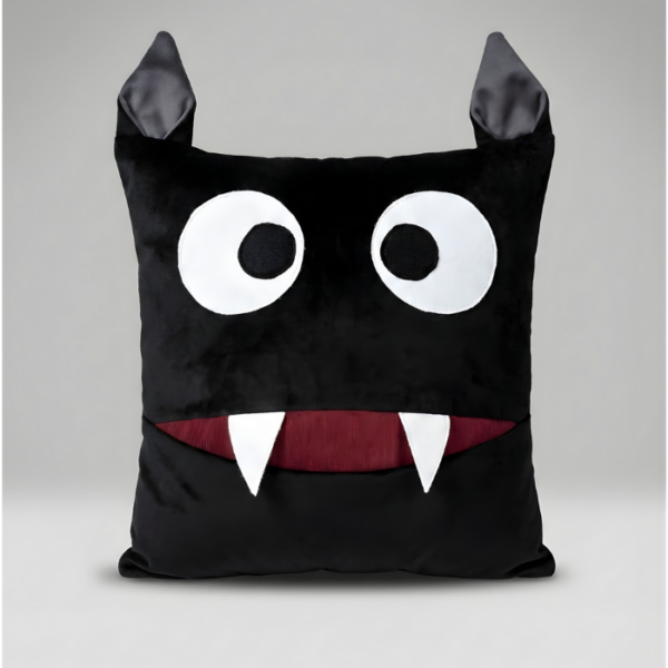A square black plush monster pillow with two pointy ears on top. It features large, surprised white eyes and a wide mouth with a deep red interior and two sharp white fangs. The mouth functions as a pocket for storage.